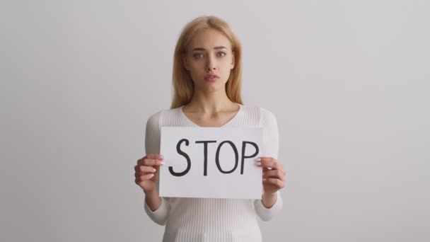 Stop vrouwelijke discriminatie. Studio portret van jonge ongelukkige vrouw poseren met poster STOP over witte muur achtergrond - Video