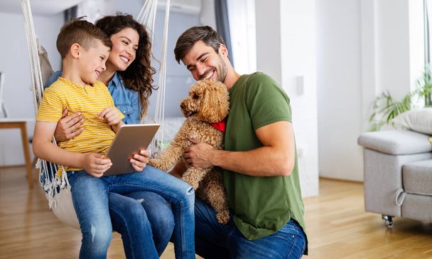 Happy young family with modern devices and dog having fun, playing at home - Foto, afbeelding