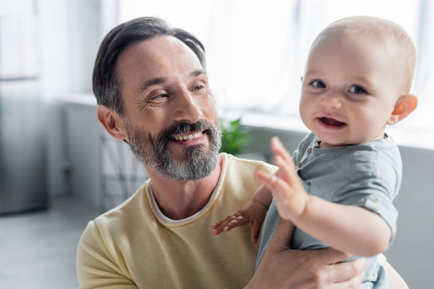 Smiling man holding baby daughter at home  - Valokuva, kuva
