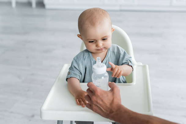 Father holding bottle with water near baby on high chair  - Φωτογραφία, εικόνα