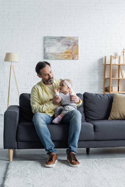 Mature man holding toddler kid on couch  - Foto, imagen