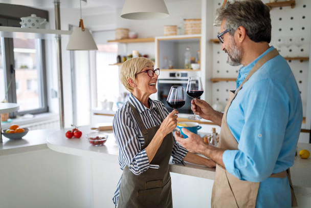 Happy senior couple having fun, cooking and drinking wine in home kitchen - Фото, зображення