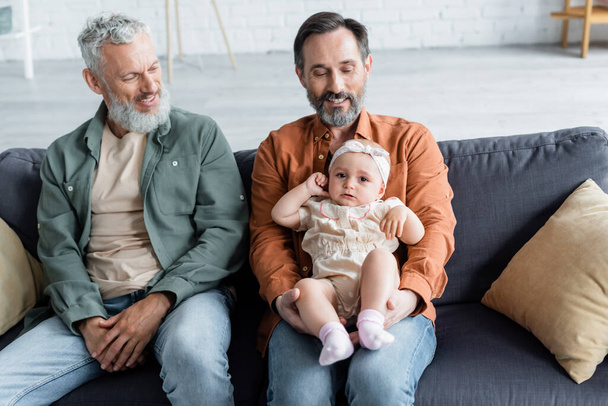 Lächelndes gleichgeschlechtliches Paar mit Tochter auf Couch  - Foto, Bild