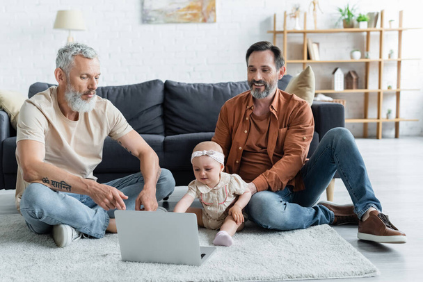 Smiling homosexual man sitting near daughter, laptop and partner  - 写真・画像