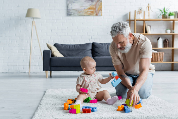 Mature father playing building blocks with child on carpet  - Valokuva, kuva