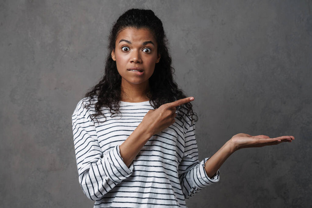 Shocked african casual brunette woman standing over gray wall background, presenting copy space - Фото, зображення
