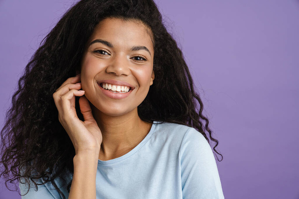 Young black woman with curly hair smiling and looking at camera isolated over purple background - Foto, Imagem