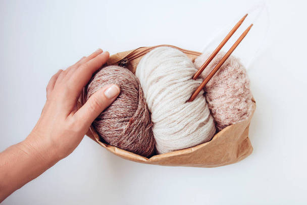 Woman's hand holds a craft eco bag with skeins of yarn in nude colors and knitting needles on a white background. Copy space. Knitwear as a concept of female hobby. Front view - Foto, immagini