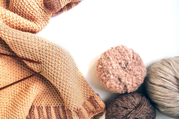 Bolas de fios de lã de cores diferentes e um suéter bege de malha, agulhas de tricô em um fundo branco. Roupas de lã feitas à mão. Passatempo tradicional. Espaço de cópia - Foto, Imagem