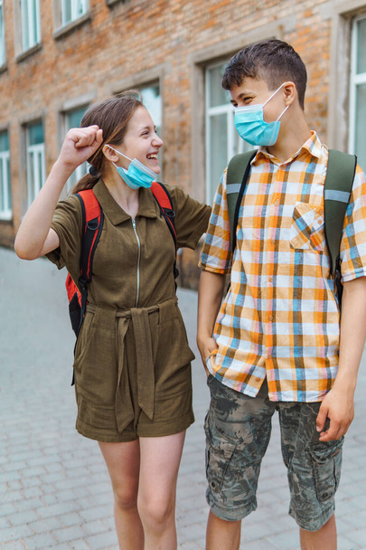 Schoolboy and schoolgirl posing on the way to school. They play, laugh and fool around. Wearing a protective mask on their faces from a coronavirus infection. Education and back to school concept. - Photo, Image