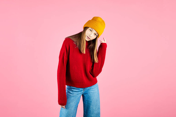 Happy young woman wearing warm sweater and knitted hat on pink background. Smiling hipster with braces having fun. - 写真・画像