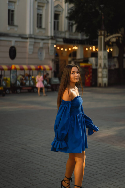 Portrait happy young woman wearing blue dress laughing looking at camera standing on street. Urban background - Fotoğraf, Görsel