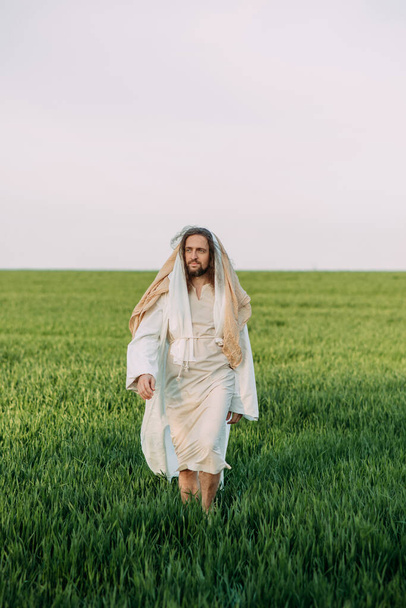 Jesus Christ walking in meadow clothed in his traditional white robe against sky background. - Photo, Image