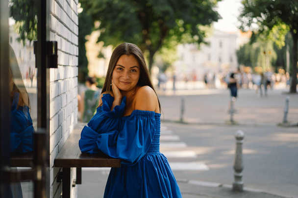 Retrato mujer joven feliz vistiendo vestido azul riendo mirando a la cámara de pie en la calle. Fondo urbano - Foto, imagen