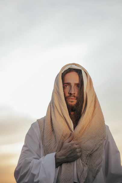 Jesus Christ stands in his traditional white robe against sky background. Portrait. - Foto, Bild