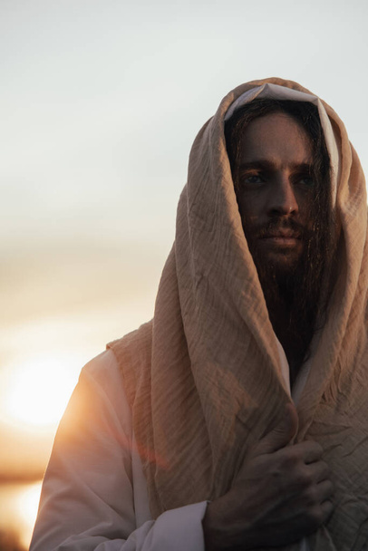 Portrait of Jesus Christ in his traditional white robe against sunset sky background. - Photo, Image