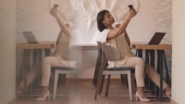 Plan complet de la jeune femme moderne assise à table dans le restaurant seul, prenant selfie avec caméra smartphone, posant - Séquence, vidéo