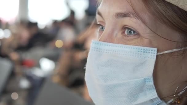 Close-up, een vrouwelijke toerist trekt een medisch masker over haar neus in een drukke luchthaven wachtkamer - Video