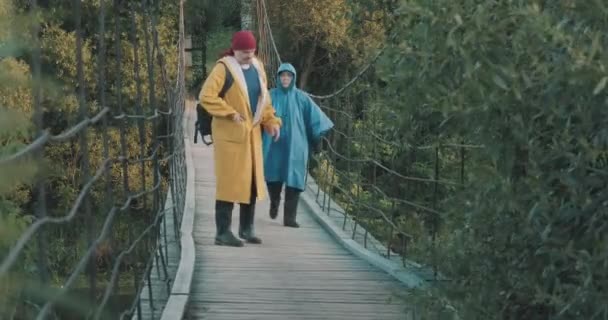 Hombre y mujer es senderismo están caminando en puente colgante mirar la ruta en gadget - Imágenes, Vídeo