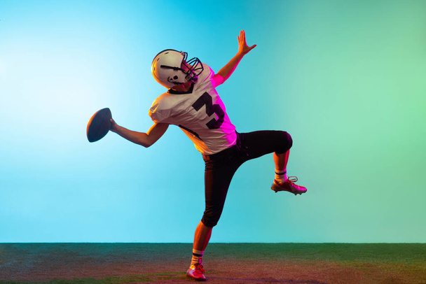 Portrait of American football player training isolated on blue studio background in neon light. Concept of sport, competition - Fotografie, Obrázek