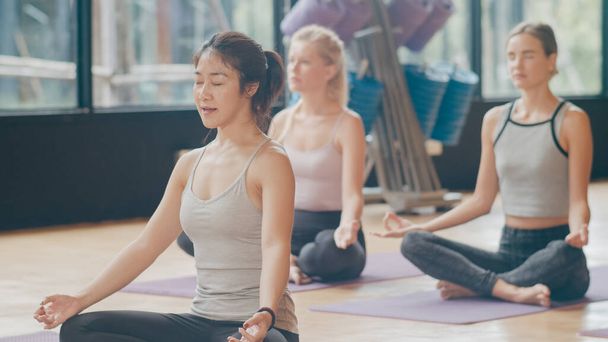 Genç, sportif insanlar eğitmenleriyle yoga dersi alıyor. Fitness stüdyosunda sağlıklı yaşam tarzı uygulayan çok ırklı bir grup kadın. Spor aktivitesi, jimnastik ya da bale dersi. - Fotoğraf, Görsel