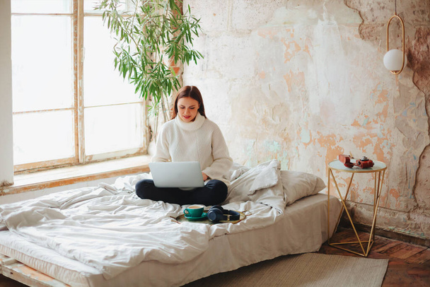 Ενθουσιασμένος ελεύθερος επαγγελματίας γυναίκα κάθεται στο κρεβάτι στο σπίτι και εργάζονται για το έργο σε απευθείας σύνδεση κατά την περιήγηση netbook  - Φωτογραφία, εικόνα