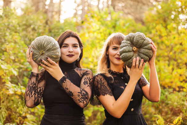 Twee vriendinnen met enge groene pompoenen voor haar gezicht, geïsoleerd boven de herfstbosachtergrond. Herfstvakantie, Halloween decoraties en mensen concept - Foto, afbeelding