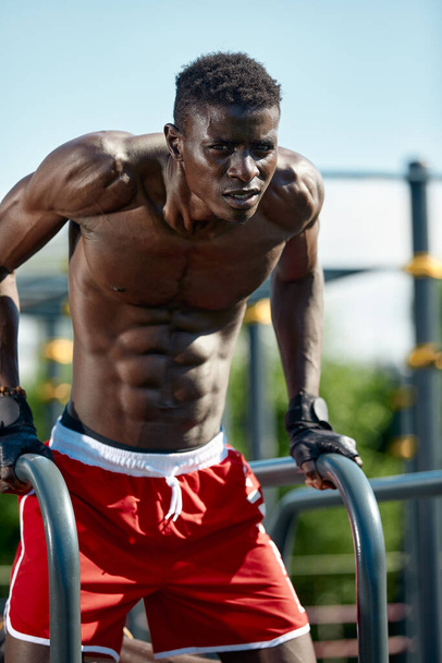 Homme de fitness noir faisant des plongées, entraînement croisé de modèle masculin en milieu urbain. Un Africain dans la vingtaine s'entraîne dans la rue. - Photo, image