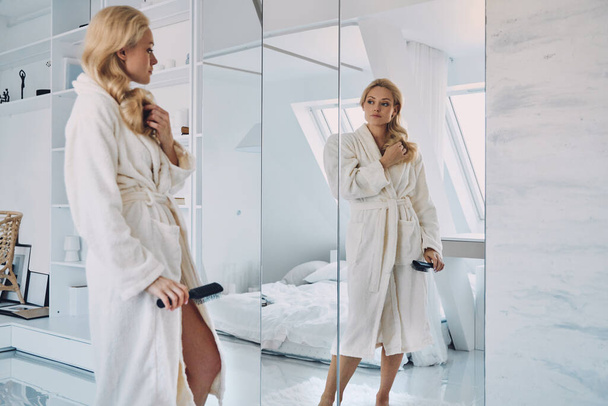 Attractive young woman in bathrobe looking at her reflection in the mirror - Foto, immagini