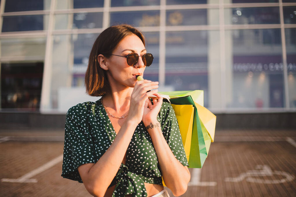 Woman at sunset with colorful shopping bags and coffee smoking enjoying  electronic cigarette - Foto, Imagen
