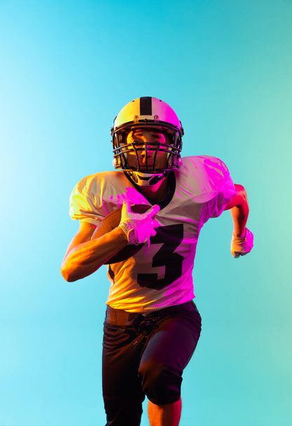 Close-up male American football player training isolated on blue studio background in neon light. Concept of sport, competition - Фото, изображение