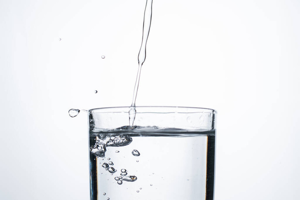 Реактивный поток воды или спирта наливается в стакан с брызгами и пузырьками, копировальное пространство. - Фото, изображение