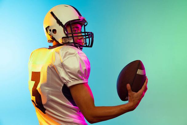 Close-up male American football player training isolated on blue studio background in neon light. Concept of sport, competition - Foto, Imagem