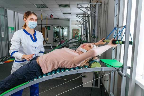 Реабилитатолог-женщина, работающая с пациенткой над специальным реабилитационным устройством - Фото, изображение