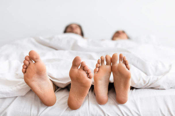 Pies de las parejas debajo de la manta mientras duermen en el dormitorio, primer plano - Foto, imagen