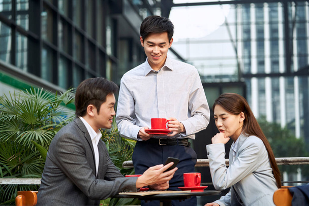 3人のアジア人ビジネスマンが屋外のコーヒーショップでビジネスについて話し合い笑顔で - 写真・画像