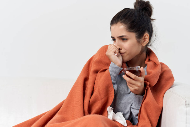 woman hiding with a plaid at home with a cup of tea treating infection - Фото, изображение