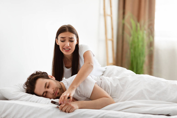 Ревнивая подружка проверяет телефон парня, пока он спит дома - Фото, изображение
