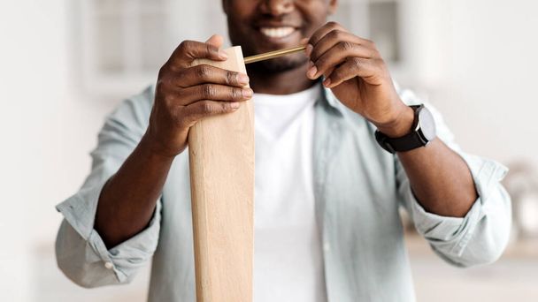 Happy african american man screwing bolt to wooden table, installing desk by yourself at home, closeup, crop - Foto, immagini