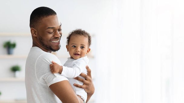 Vater und Baby. Porträt eines glücklichen schwarzen Millennial-Vaters, der ein Kleinkind in den Armen hält - Foto, Bild