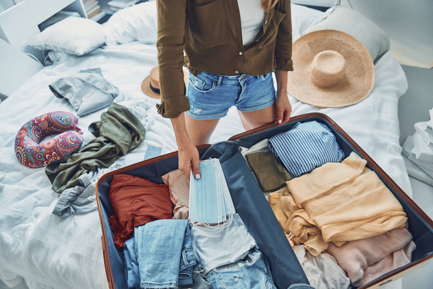 Beautiful young woman packing luggage while sitting in bed at home - Zdjęcie, obraz