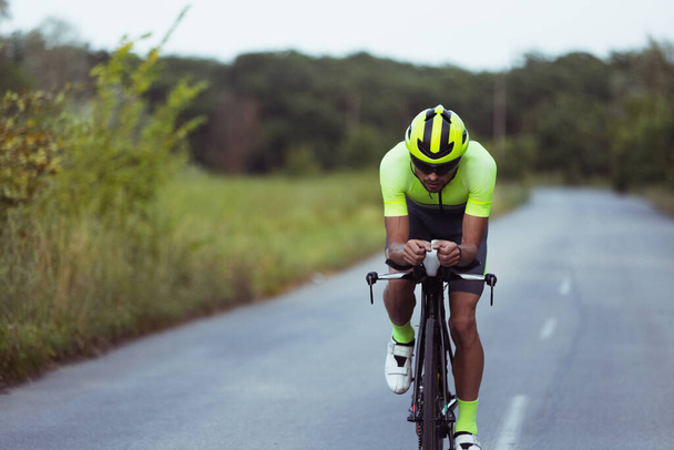 Νεαρός τριαθλητής με ποδήλατο στον ανοιχτό δρόμο. Επαγγελματίας αθλητής συμμετέχει σε τρίαθλο τη φωτεινή καλοκαιρινή ημέρα - Φωτογραφία, εικόνα
