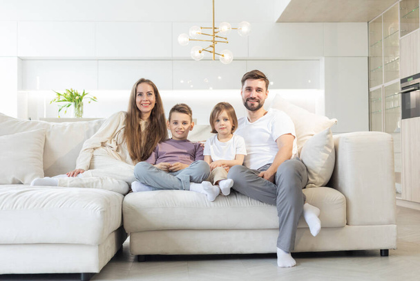 Family portrait of young parents with their two children at home, white modern desgin of living room - Фото, зображення