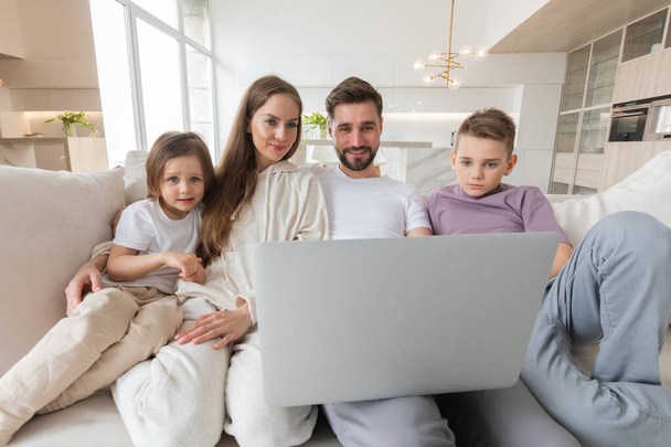 Portrait of family of parents with their two children relaxing in living room sitting together browsing internet on laptop computer - Valokuva, kuva
