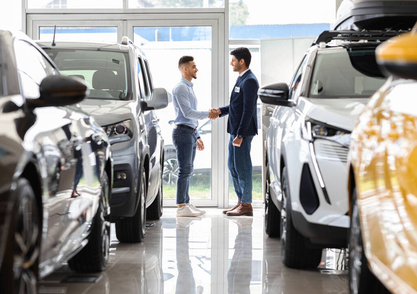 Rico hombre de Oriente Medio sacudiendo gerente de ventas mano en sala de exposición de automóviles - Foto, Imagen