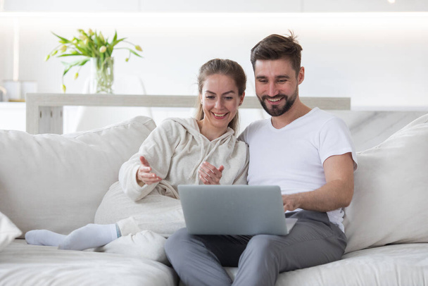 Porträt eines erwachsenen Paares, das es sich im Wohnzimmer gemütlich macht und zusammen am Laptop im Internet surft - Foto, Bild