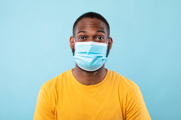 Porträt eines Afroamerikaners mit antiviraler Maske vor blauem Studiohintergrund. Stopp des komischen Konzepts - Foto, Bild