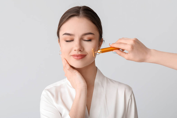 Mulher bonita com ferramenta de massagem facial no fundo claro - Foto, Imagem