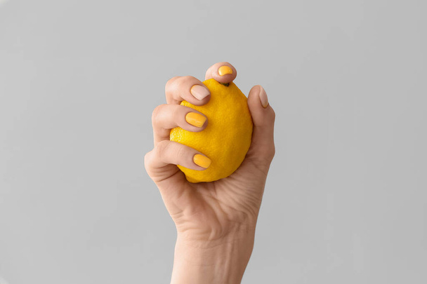 Žena ruka s krásnou manikúru a citron na šedém pozadí - Fotografie, Obrázek