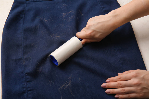 Woman cleaning clothes with lint roller on light background, closeup - 写真・画像